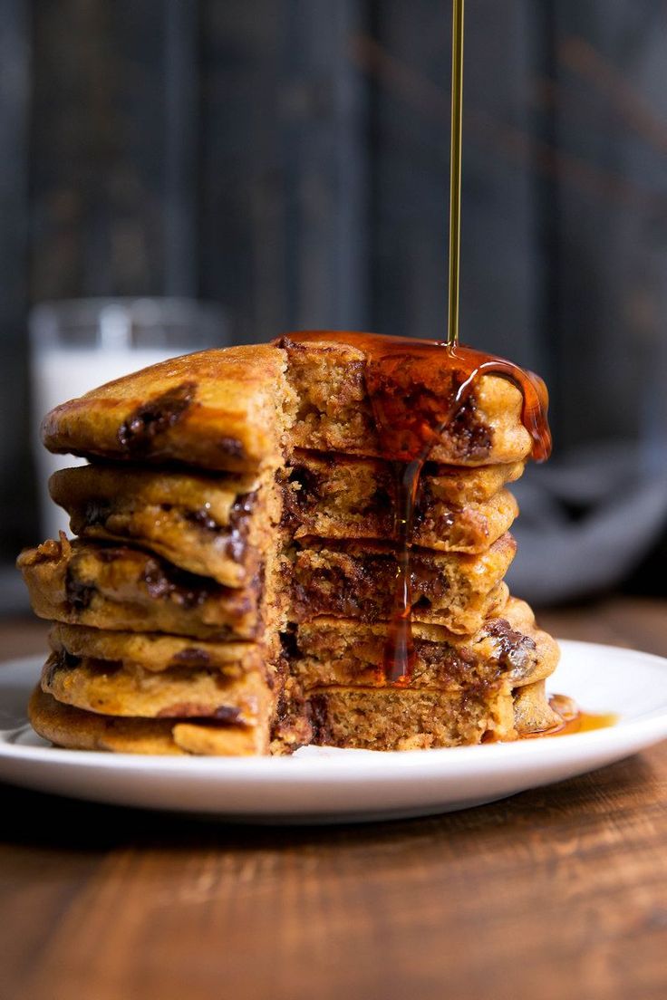 stack of pancakes with syrup being drizzled over them on a white plate