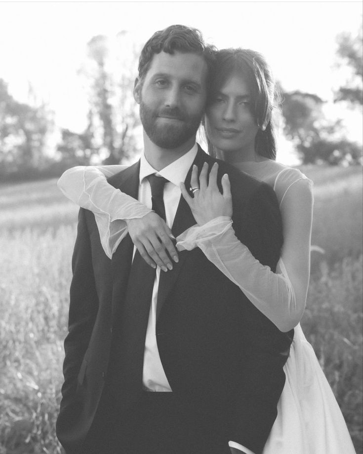 black and white photograph of a bride and groom hugging each other in the middle of a field