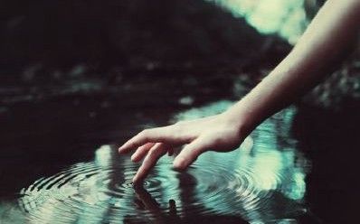 a person's hand reaching for something in the water that is reflecting it on its surface