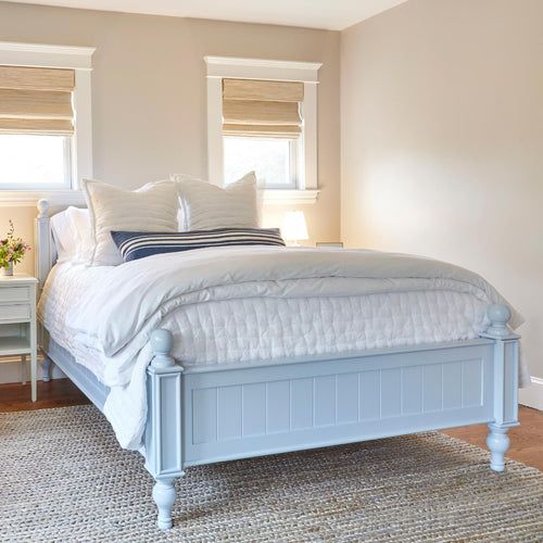 a white bed sitting next to two windows in a bedroom on top of a rug