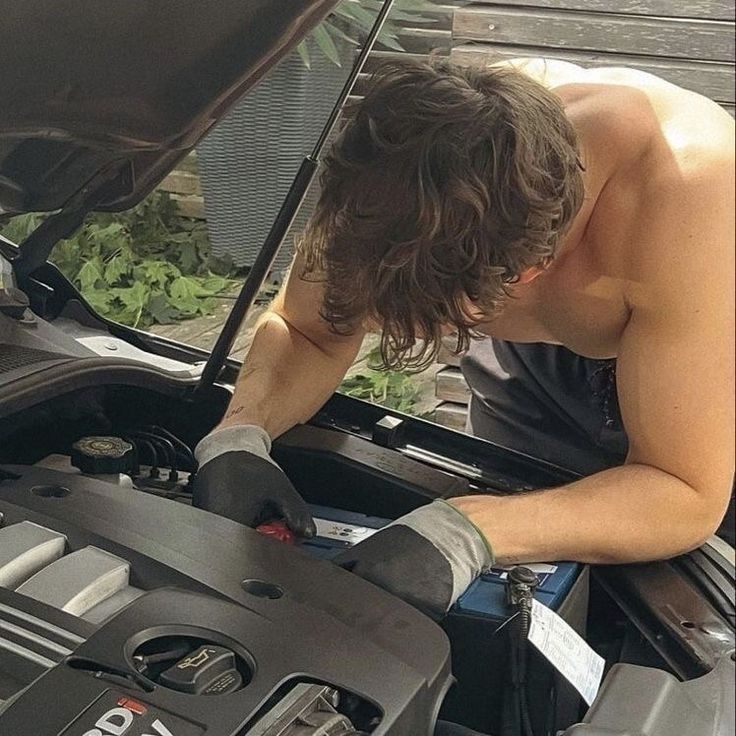 a man working on an engine in the hood of a car while looking at it