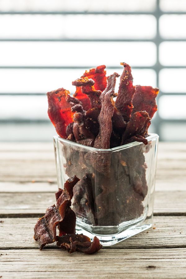 a glass bowl filled with dried red peppers on top of a wooden table next to a window