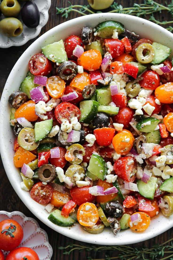 a large bowl filled with lots of different types of vegetables next to olives and tomatoes