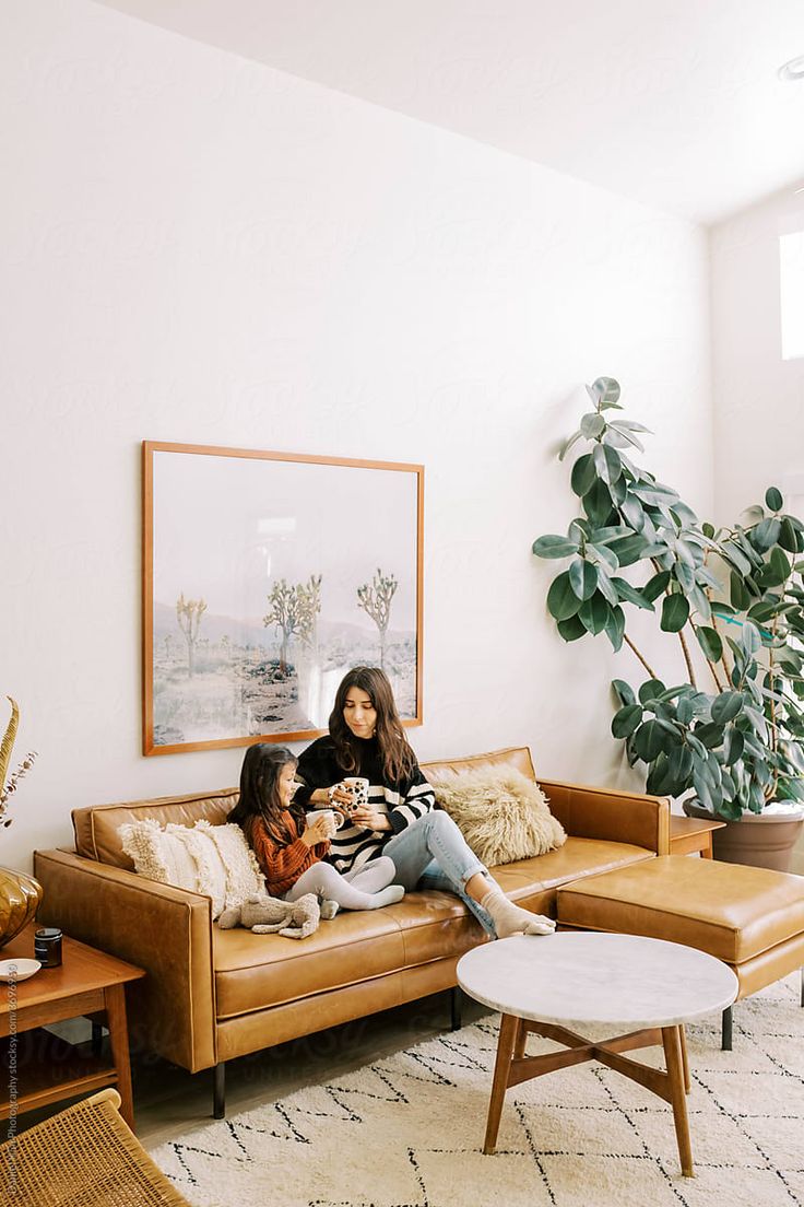 two women sitting on a couch in front of a potted plant and coffee table