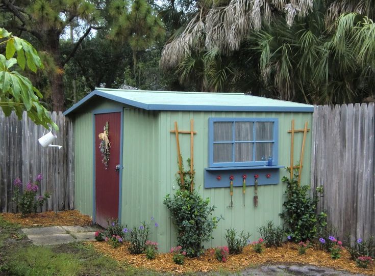 a small green shed with plants growing around it