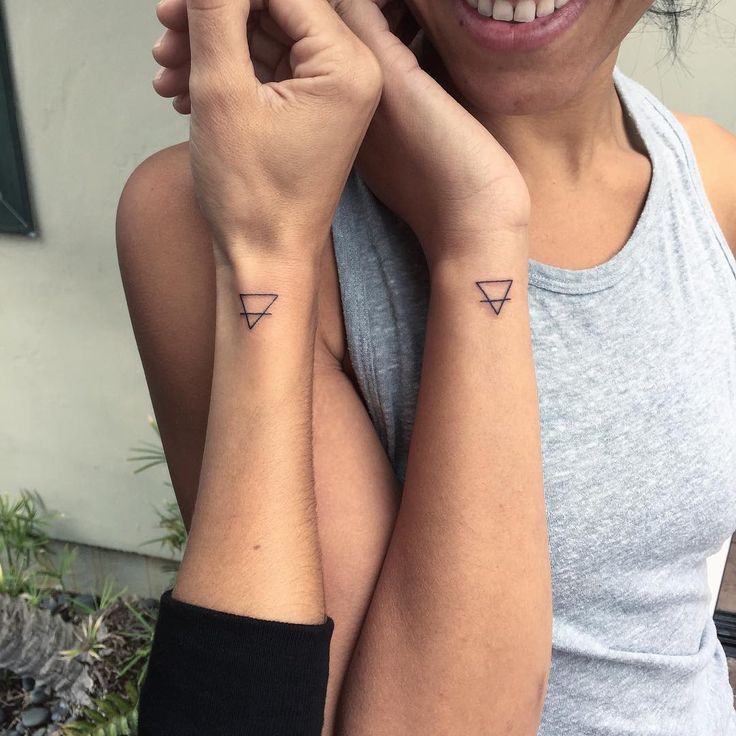 two women with matching tattoos on their arms, one holding the other's hand