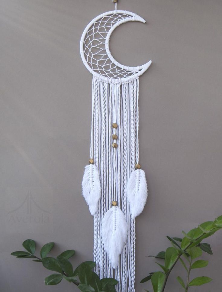 a white dream catcher hanging from the side of a gray wall next to a potted plant