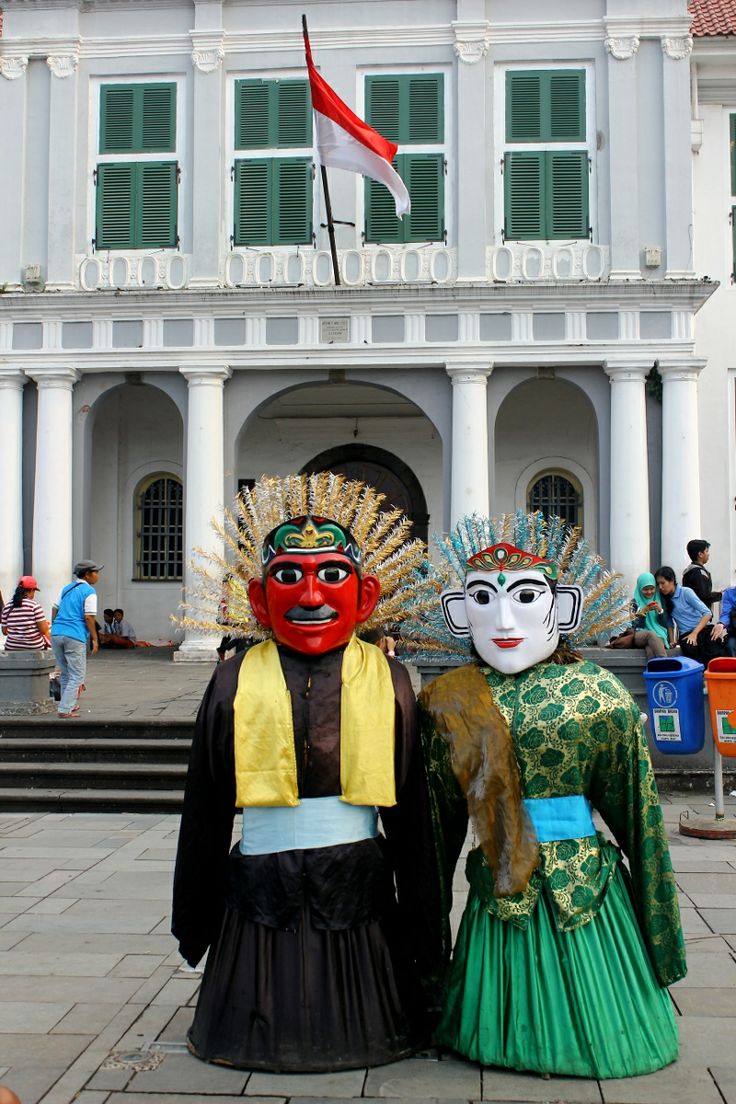 two people wearing masks standing in front of a white building with green trimmings