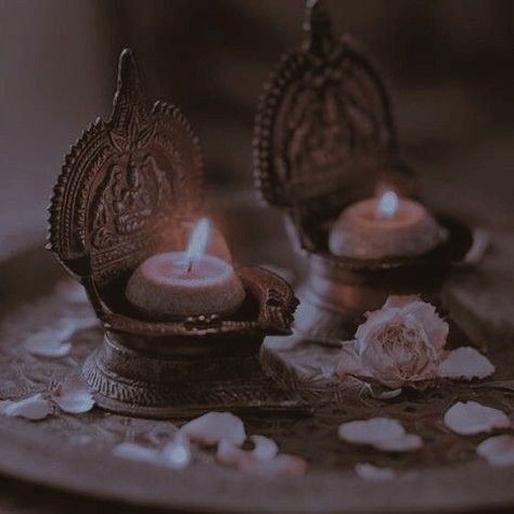 two lit candles sitting on top of a metal tray with petals scattered around the edges