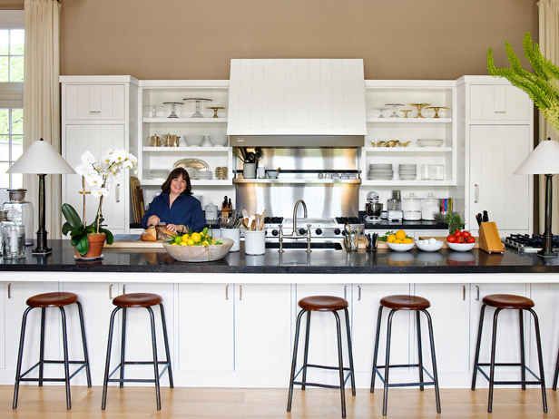 a woman standing at the counter in a kitchen with three stools next to her