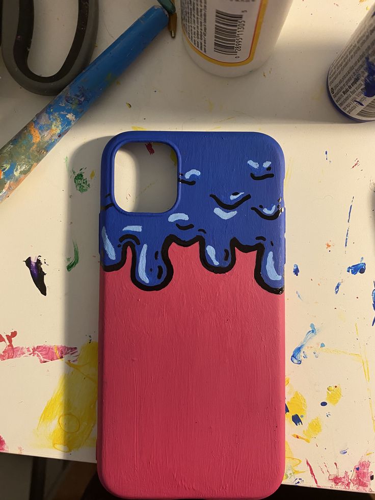 an iphone case painted with blue and pink paint sitting on top of a table next to scissors