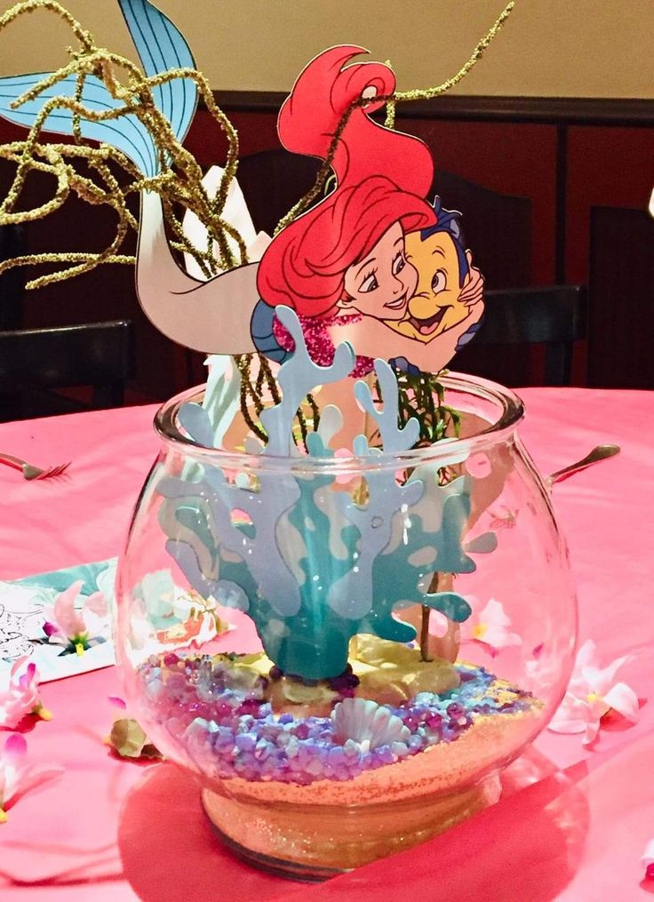 the little mermaid is in a fish bowl with seaweed and other decorations on it