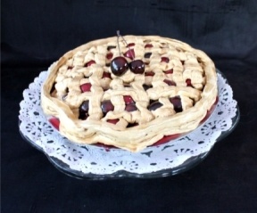 a pie with cherries on top sitting on a doily covered cake platter