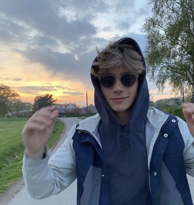 a young man wearing sunglasses and a hoodie is standing on a path with his hands in the air