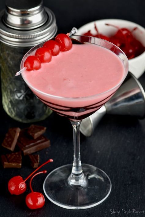 a pink drink with cherries in it sitting on a table next to some chocolate