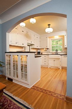 an archway in the middle of a kitchen with white cabinets and wood flooring, along with hardwood floors