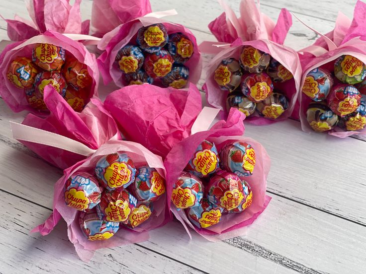 candy wrapped in pink paper sitting on top of a white wooden table next to each other