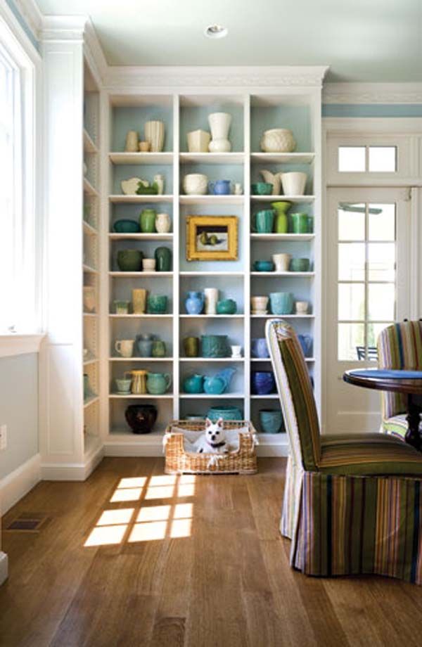 a dining room table and chairs in front of a bookshelf filled with vases