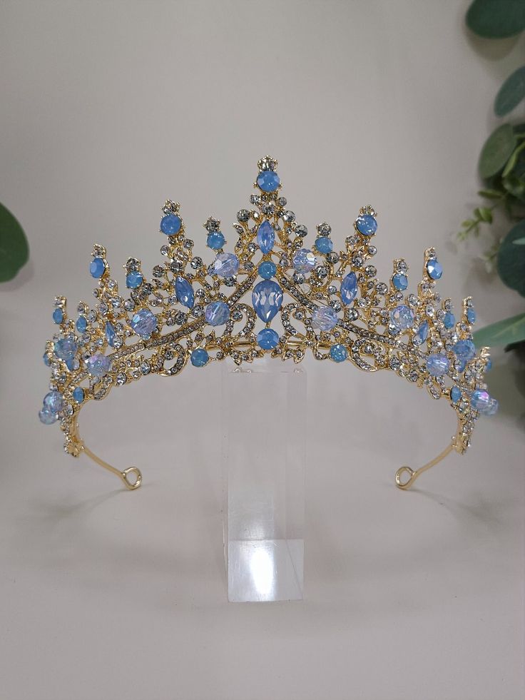 Introducing Princess our custom Gold and Light Blue Tiara - perfect for your special event! Whether it's your big day as a bride, a Quinceanera, or a pageant, this Baby Blue Gold bridal tiara will be the crowning glory of your outfit. Crafted with exquisite attention to detail and gold and blue stones, gold crystals, blue beads it's sure to add a hint of royalty to your look. Darling Princess Crown in Gold Blue Quince Crown with light Blue Stones Quinceanera Tiara Details: 2 1/2" High. Blue Bead Blue Tiara Wedding, Quince Crowns Gold And Blue, Light Blue Quince Crown, Baby Blue And Gold Quinceanera Theme, Light Blue And Gold Quince, Gold Quinceanera Crown, Quinceanera Crowns Gold, Quinceanera Crowns, Quince Crowns