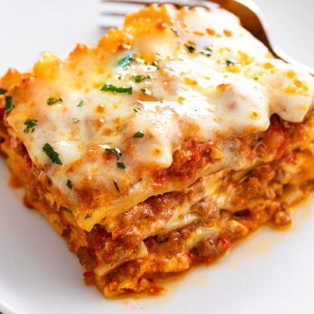 a white plate topped with lasagna covered in sauce and cheese next to a fork