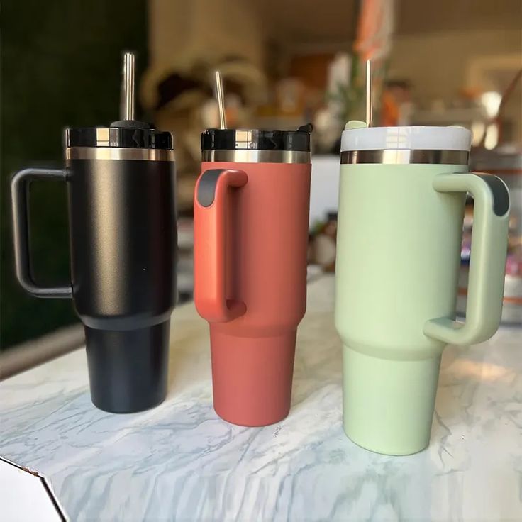 three different colored coffee cups sitting on top of a counter next to each other,