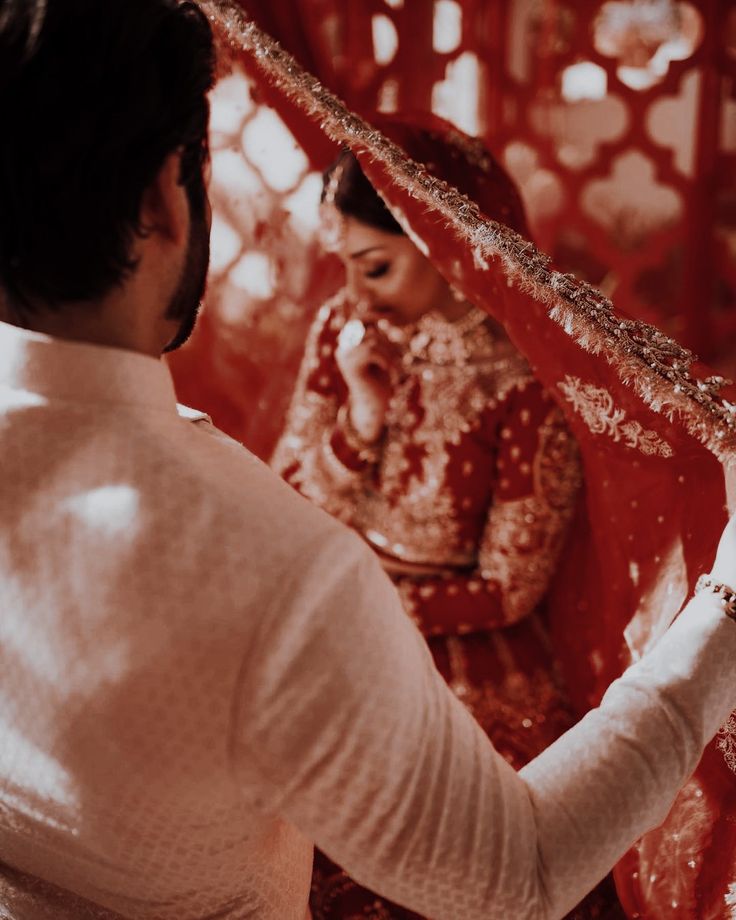 a man and woman standing next to each other in front of a red wall with intricate designs on it