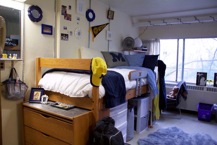 a dorm room with a bed, dresser and other items on the floor in front of a window