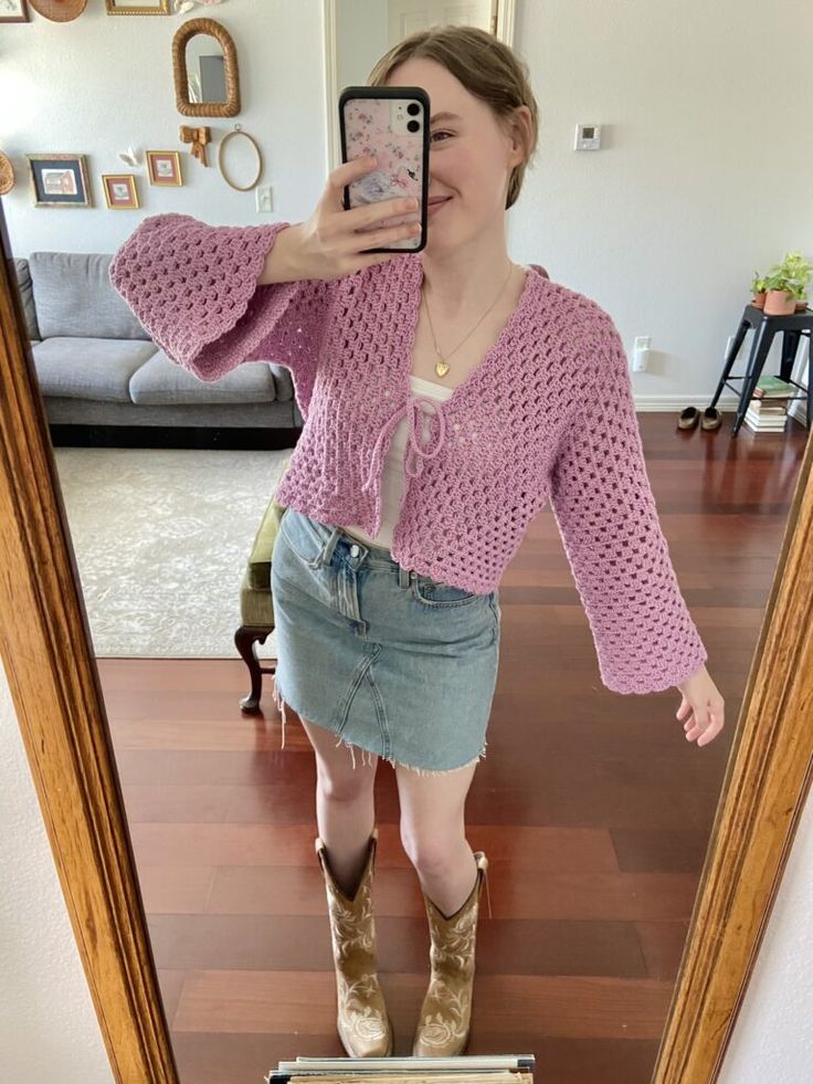 a woman taking a selfie in front of a mirror wearing boots and a pink sweater