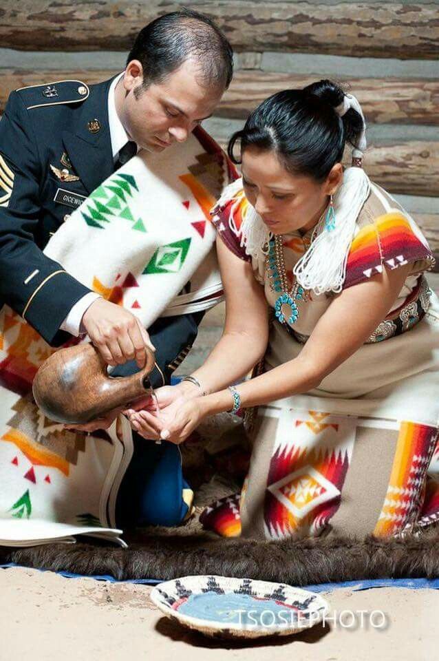 a man and woman dressed in native american clothing cutting something on the ground with scissors