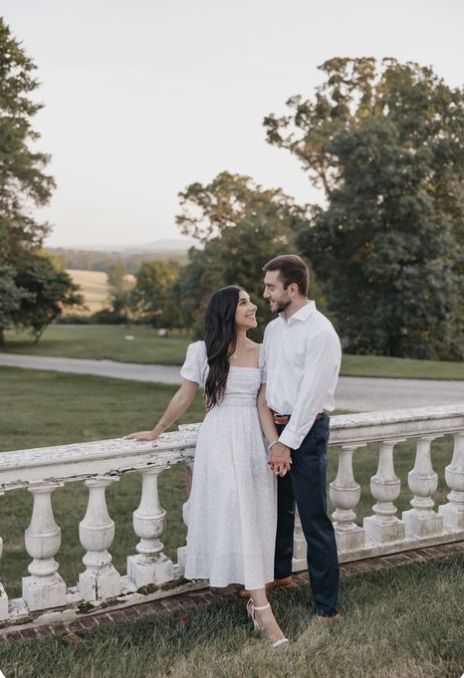 a man and woman standing next to each other in front of a white fence