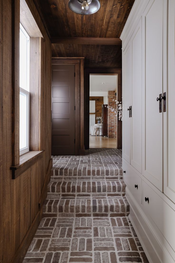 an empty hallway with wood paneling and white cabinets on either side, leading to another room