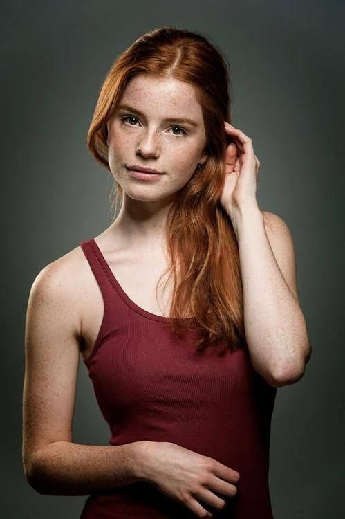 a woman with long red hair is posing for a photo in front of a gray background