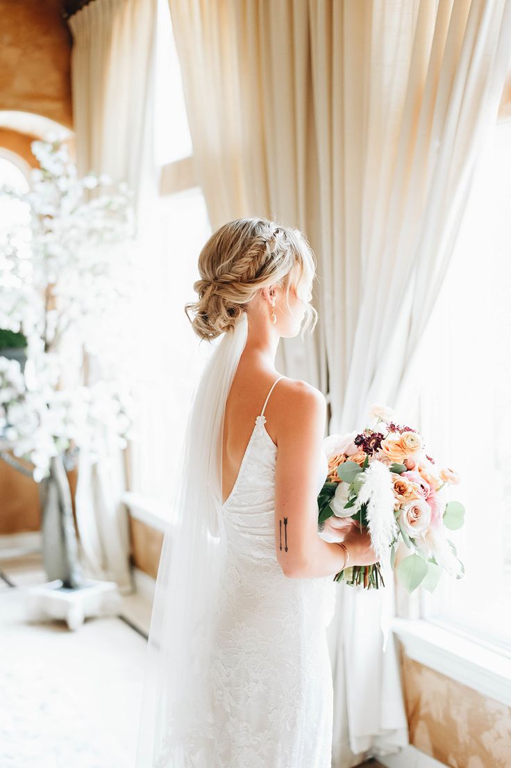 a woman in a wedding dress holding a bouquet and looking out the window at something outside