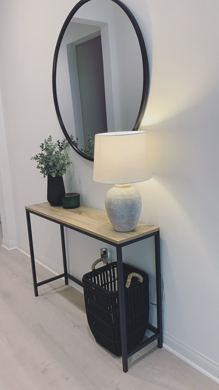 a table with a lamp, basket and mirror on it in front of a white wall