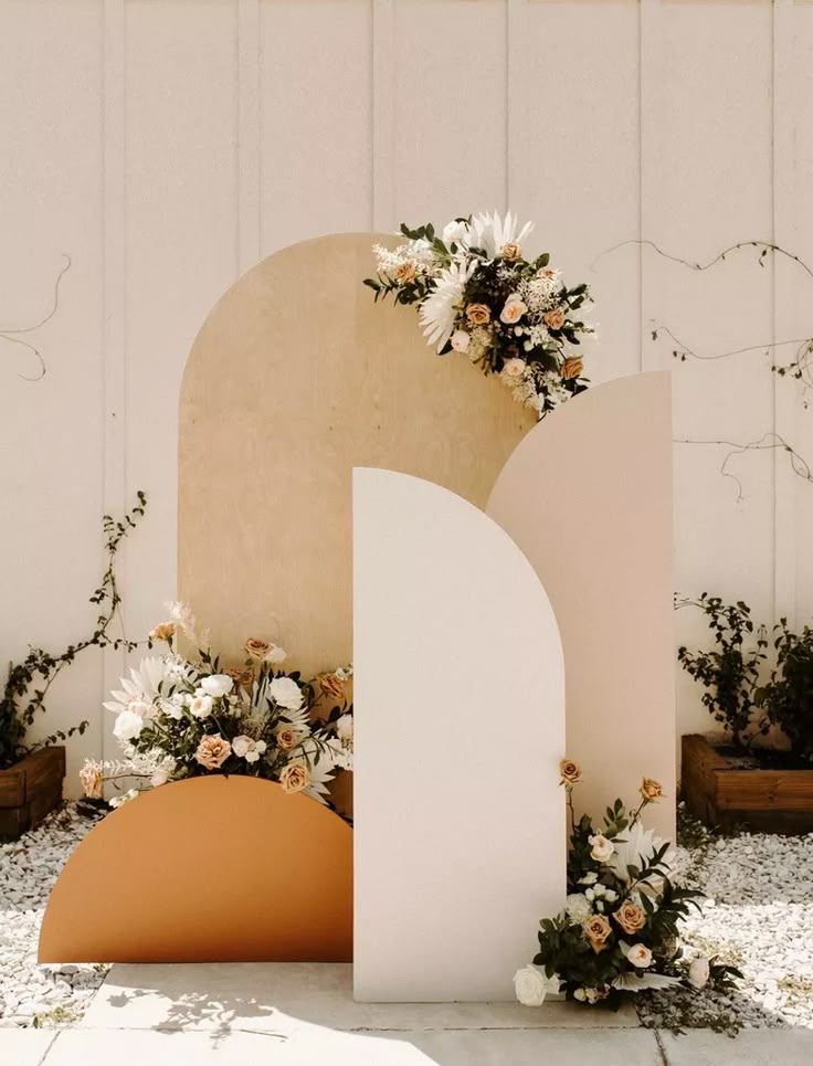 an arch with flowers on it is in front of a white wall and some plants