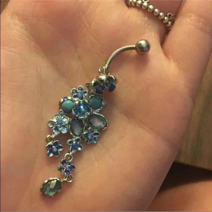 a hand holding a belly ring with flowers on it