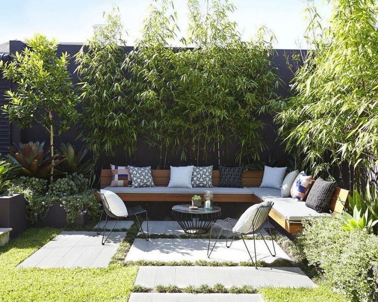 an outdoor seating area with bamboo trees and plants on the wall, surrounded by grass