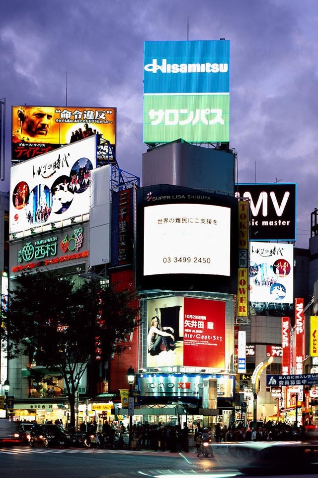 a busy city street filled with lots of tall buildings and billboards at night time