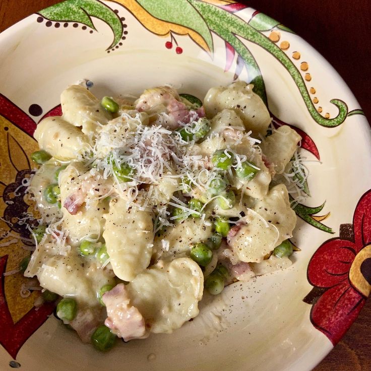 a white plate topped with pasta covered in cheese and peas on top of a wooden table