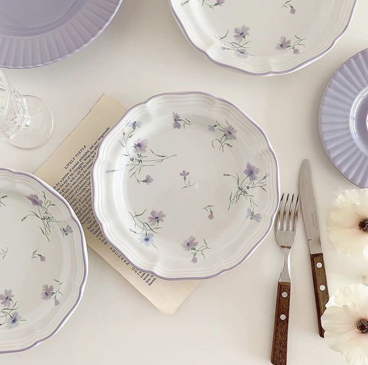 the table is set with purple and white dishes, silverware, and napkins