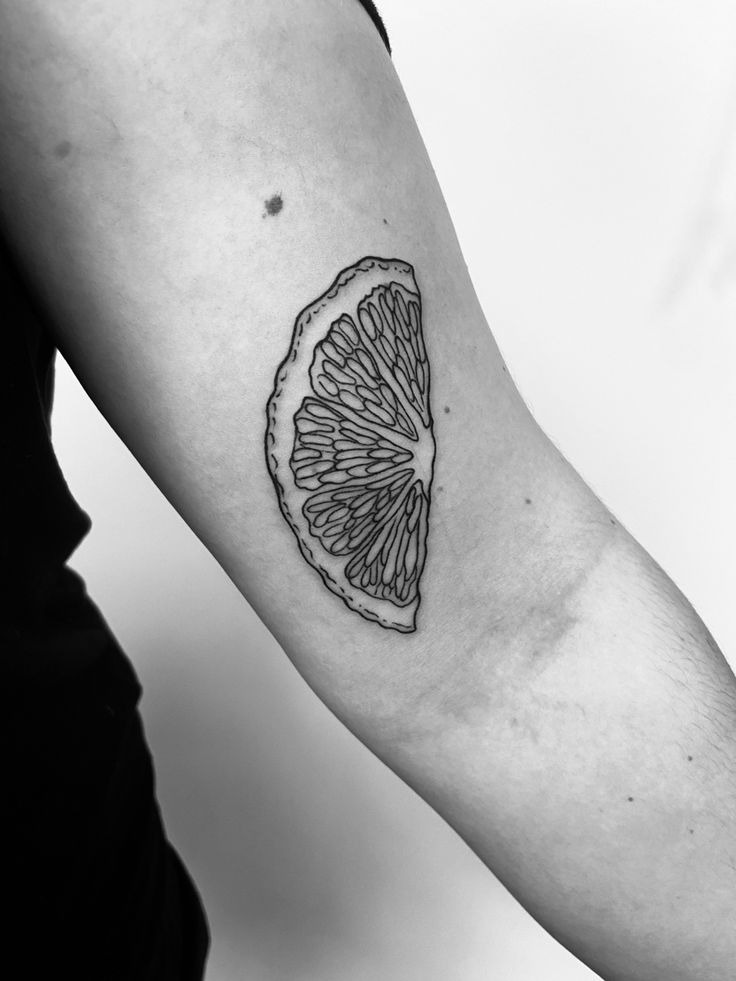 a black and white photo of a lemon slice tattoo on the right arm, which has been drawn in half