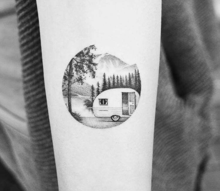 a woman's arm with a small camper in the background and trees on it