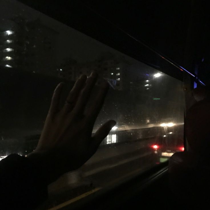 a person is holding their hand out the window at night time, with city lights in the background