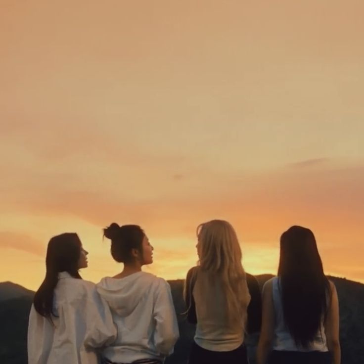 three young women standing on top of a hill at sunset