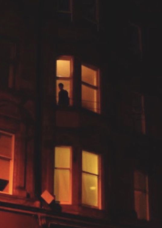 two people standing on the ledge of a building at night looking out from their windows