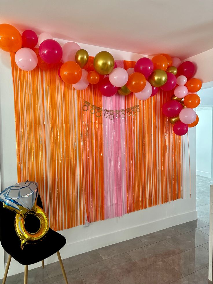 balloons and streamers are hanging from the ceiling in front of an orange curtain with gold fringes