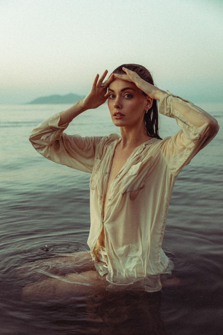 a woman is sitting in the water with her hands on her head and looking off into the distance