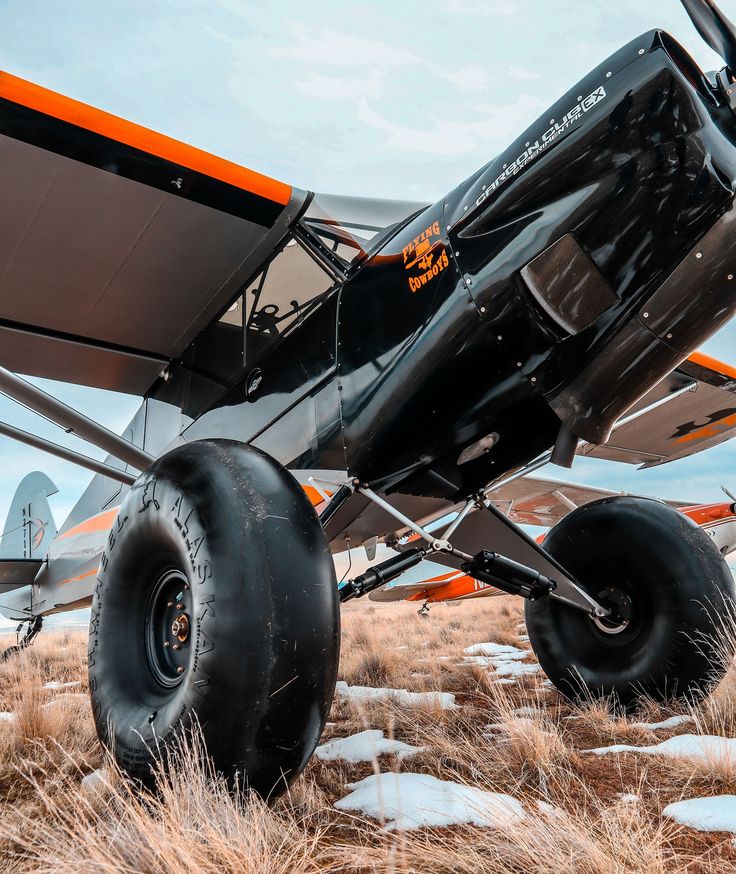 an orange and black airplane is parked in the snow with large tires attached to it