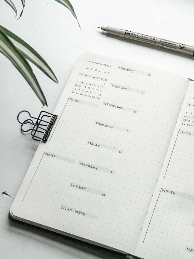 an open notebook sitting on top of a table next to a pen and plant with lots of writing