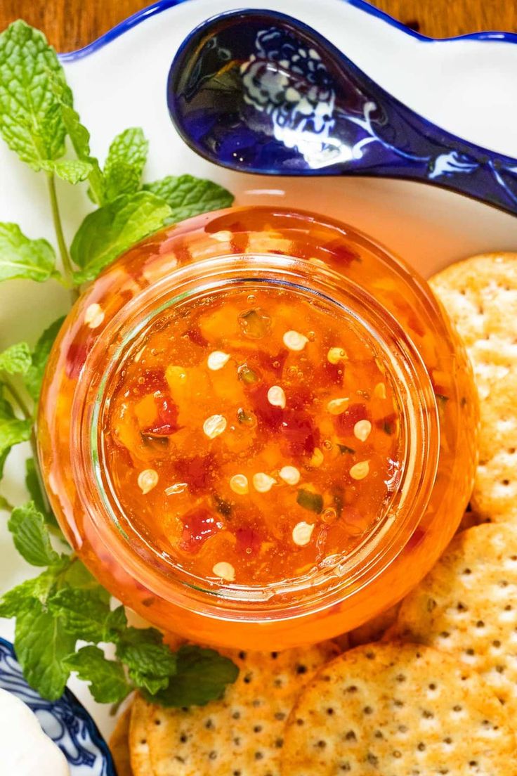 a plate with crackers and a jar of salsa on it next to a spoon